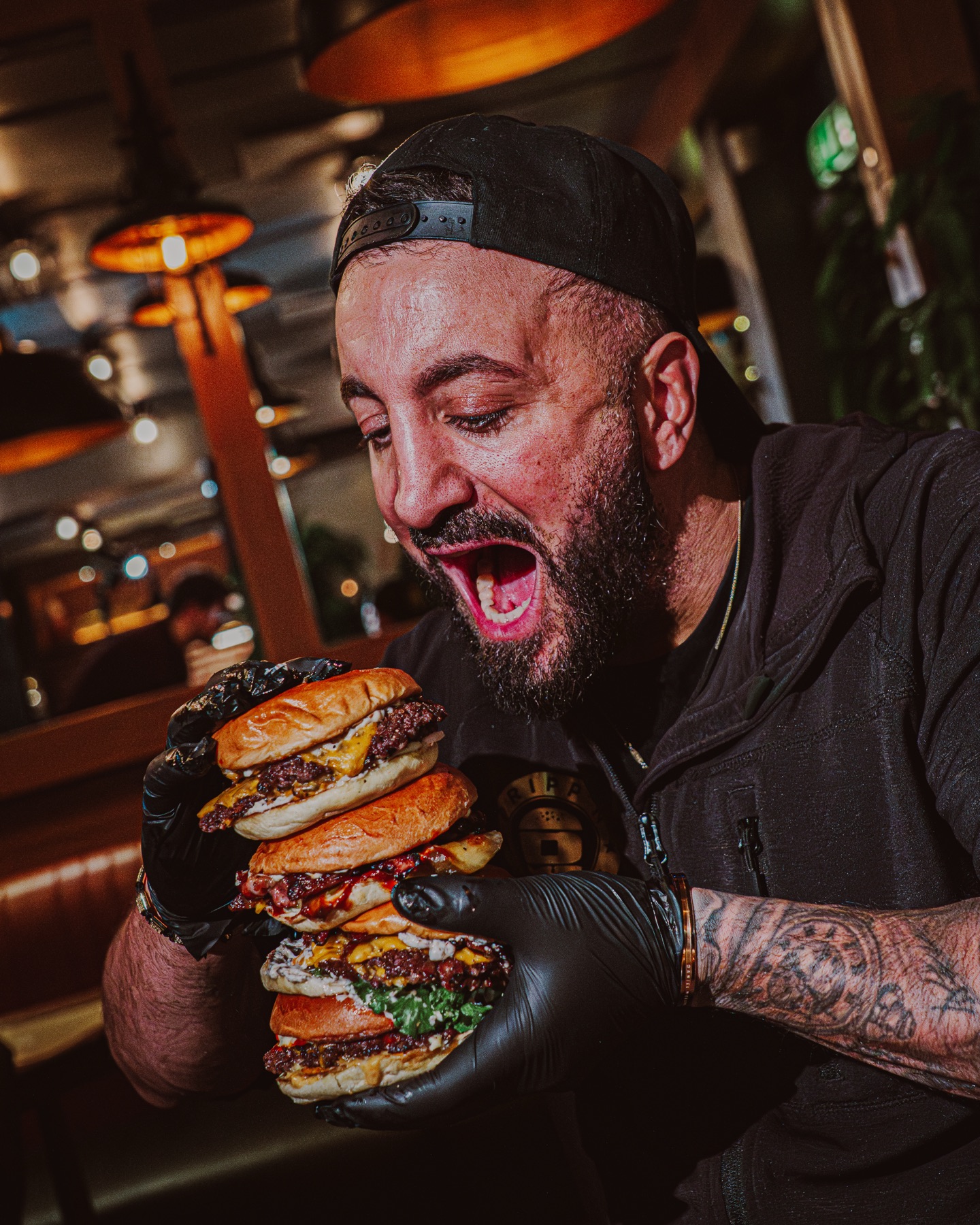 Grundaren i bakåtvänd keps gapar mot ett torn av fyra staplade smashburgare