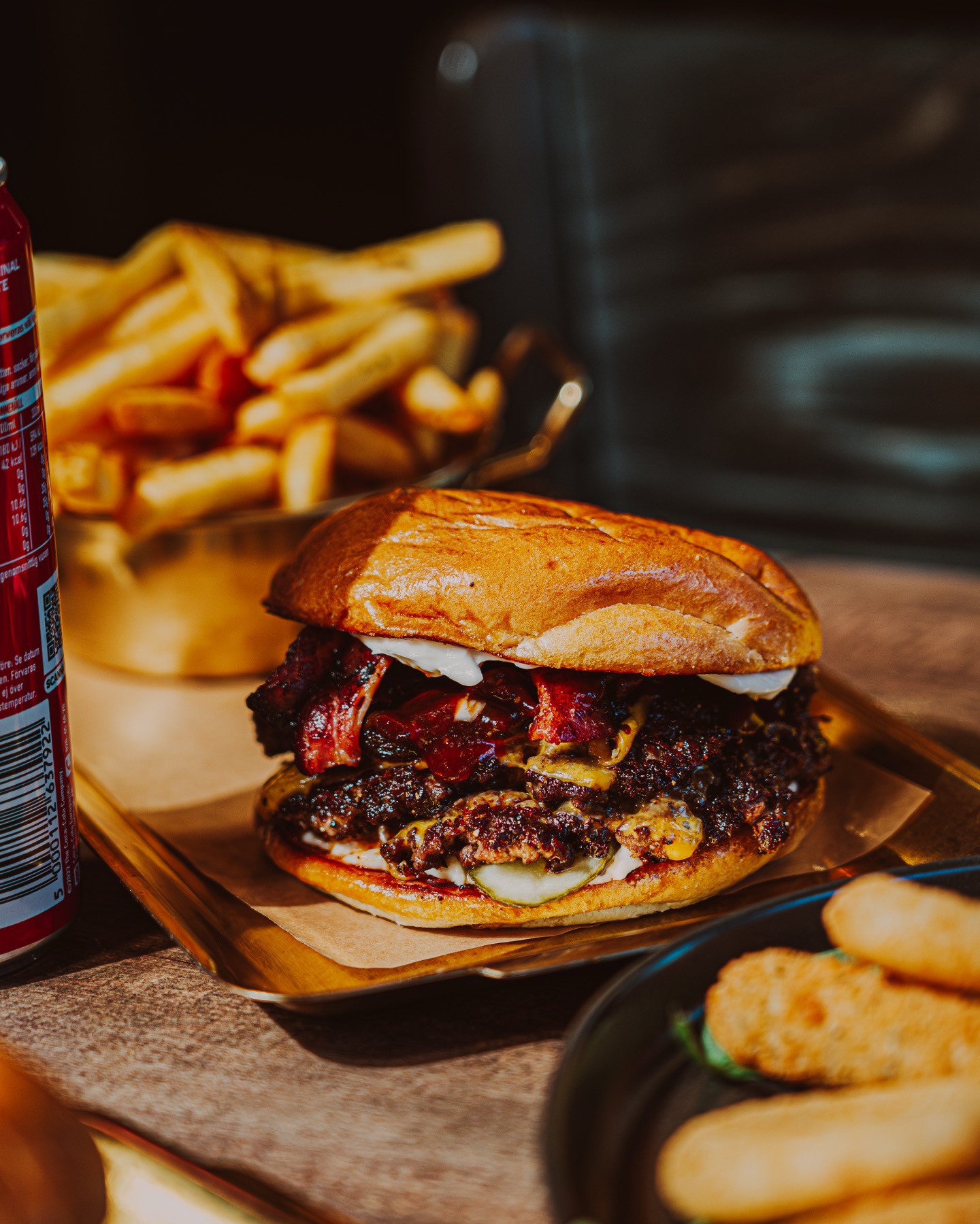 Smashburgare med bacon och smält ost serverad på mässingsbricka med pommes och läsk
